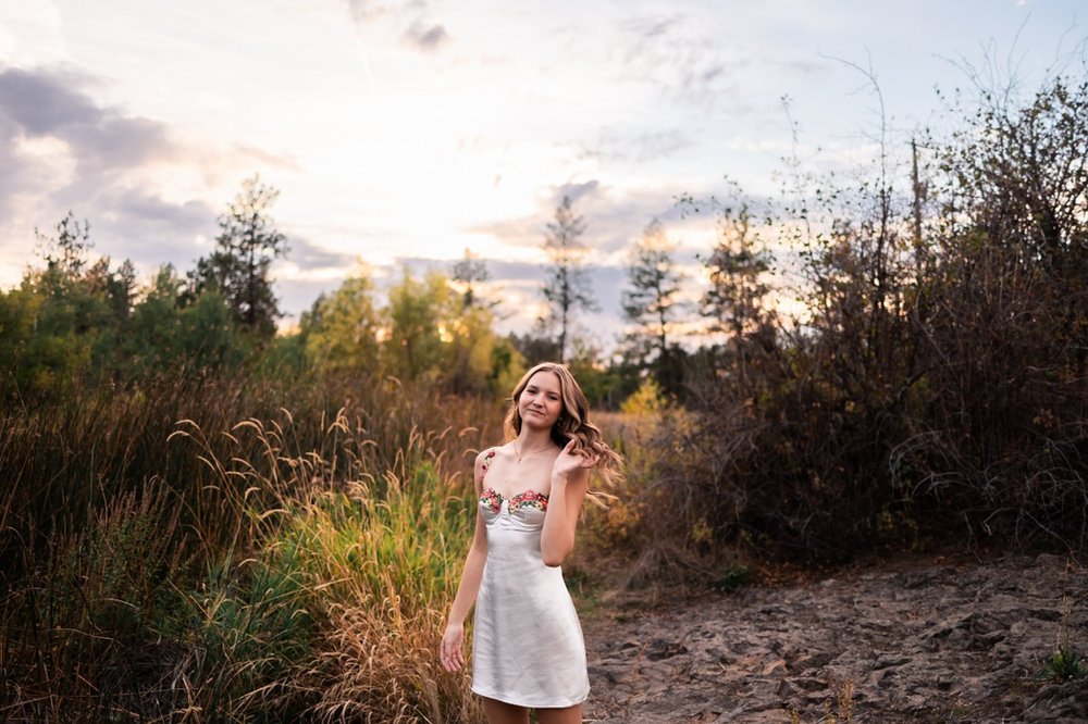 Highschool senior girl in white dress with beautiful sunset landscape behind her